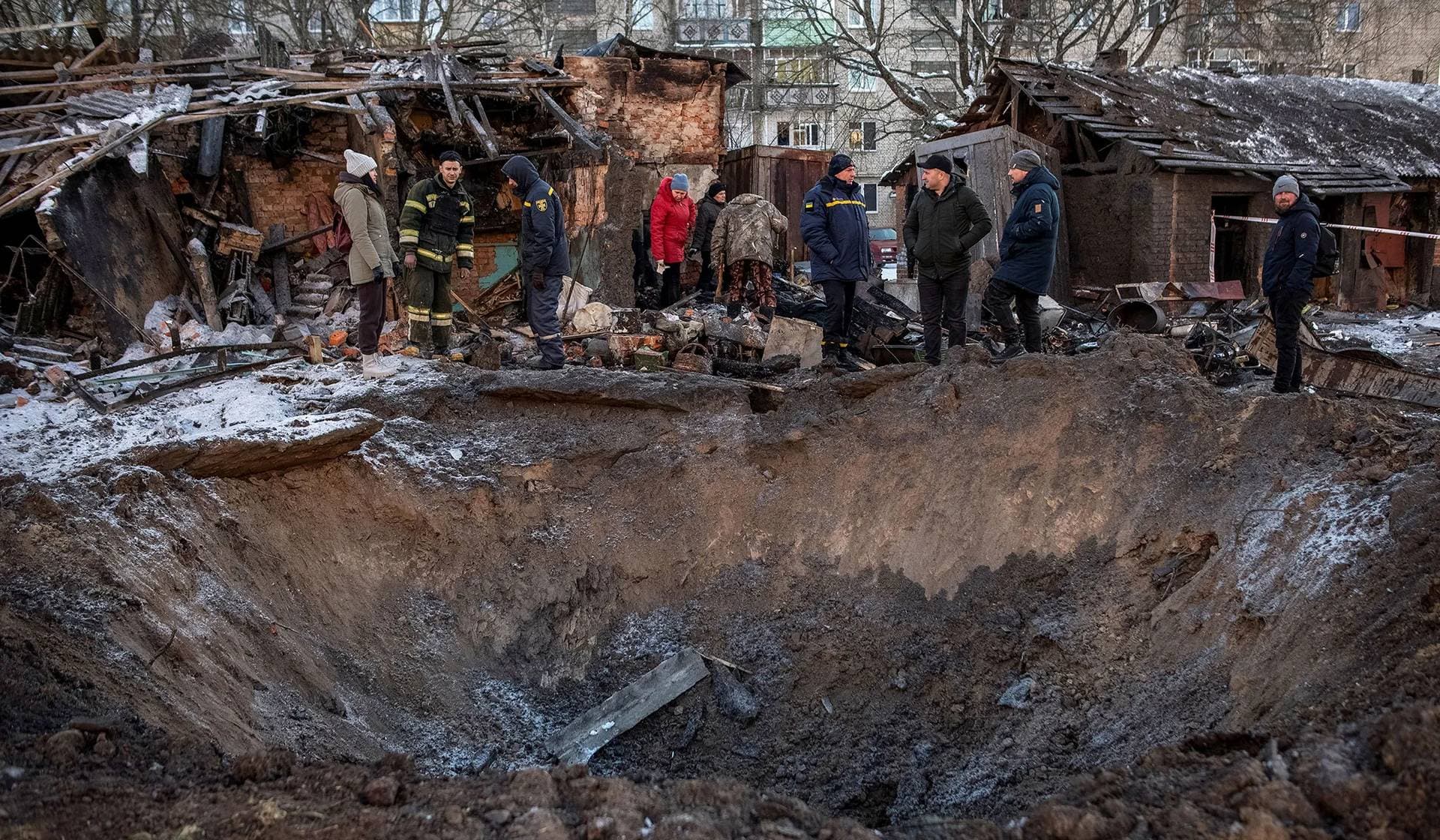 Local residents look at a crater near their residential building damaged during a Russian missile strike in Shostka