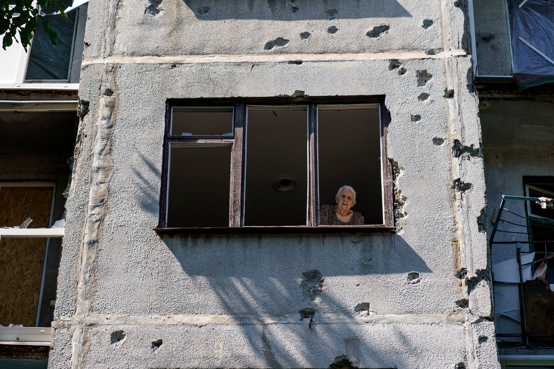 An elderly woman looks out of her apartment window in a damaged building from a May rocket attack in Sloviansk