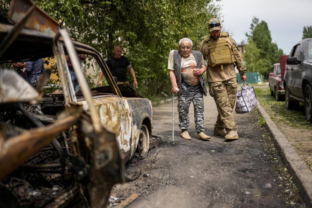 A volunteer helps a man leaving his home in a building damaged by an overnight missile strike, in Sloviansk