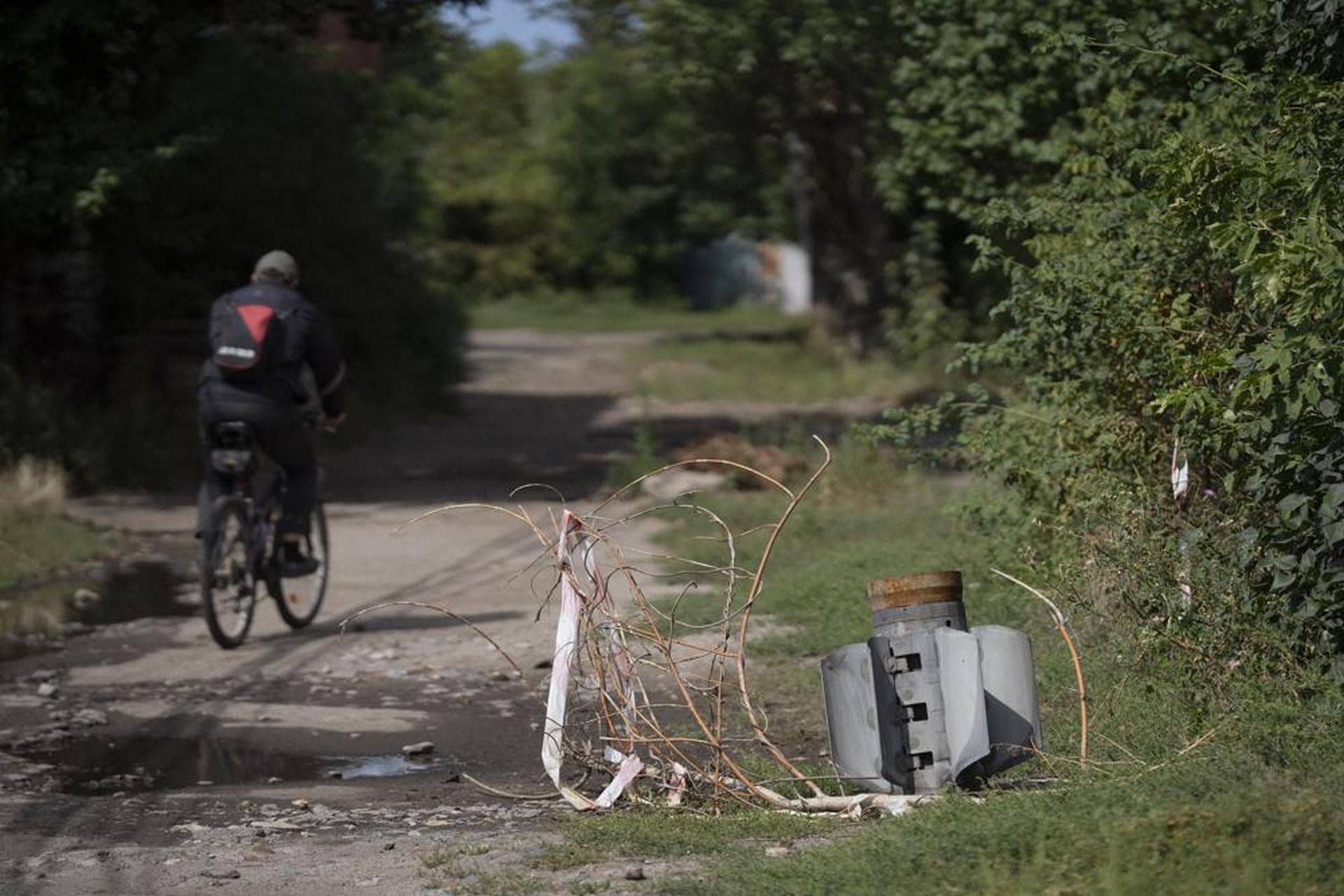 A man cycles past part of a rocket that sits wedged in the ground at a residential area in Sloviansk