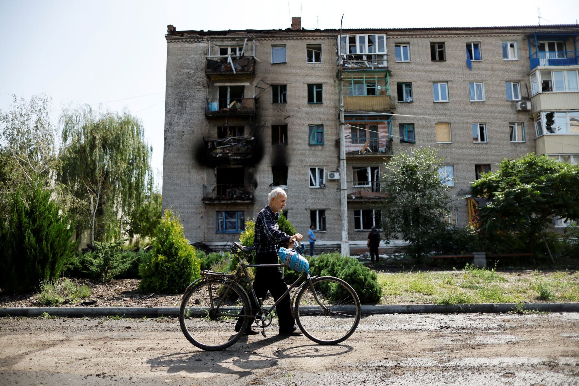 A Ukrainian man walks with his bicycle in front of damaged houses following recent Russian shelling in the city of Sloviansk