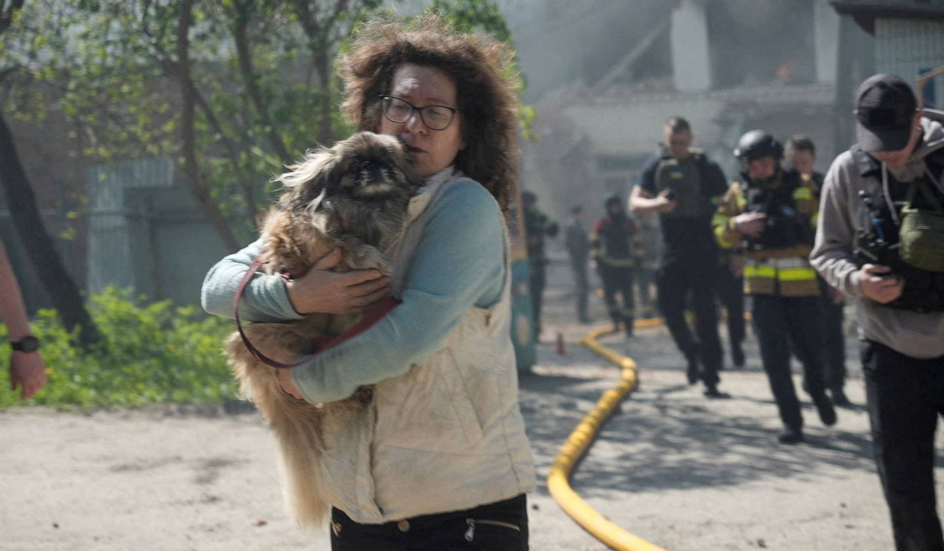 A resident with a dog and rescuers run during an air raid alarm at the site of the kindergarten hit by a Russian drone strike in Sumy