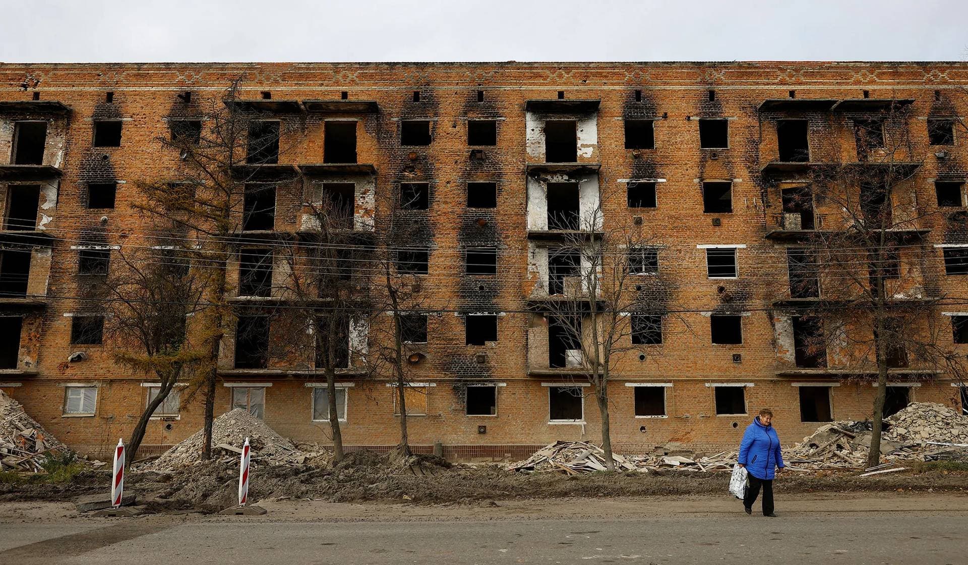 A local woman walks in front of an apartment building under reconstruction, heavily damaged on the first months of Russia's attack on Ukraine, in Trostianets