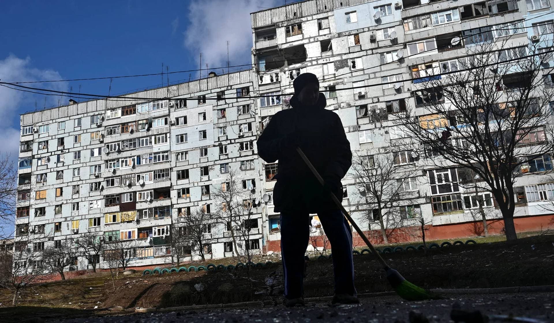 A local resident sweeps debris in front of a residential building damaged by a Russian military strike in Stepnohirsk, Vasylivka Raion, Zaporizhzhia Region, Ukraine, February 21, 2023.