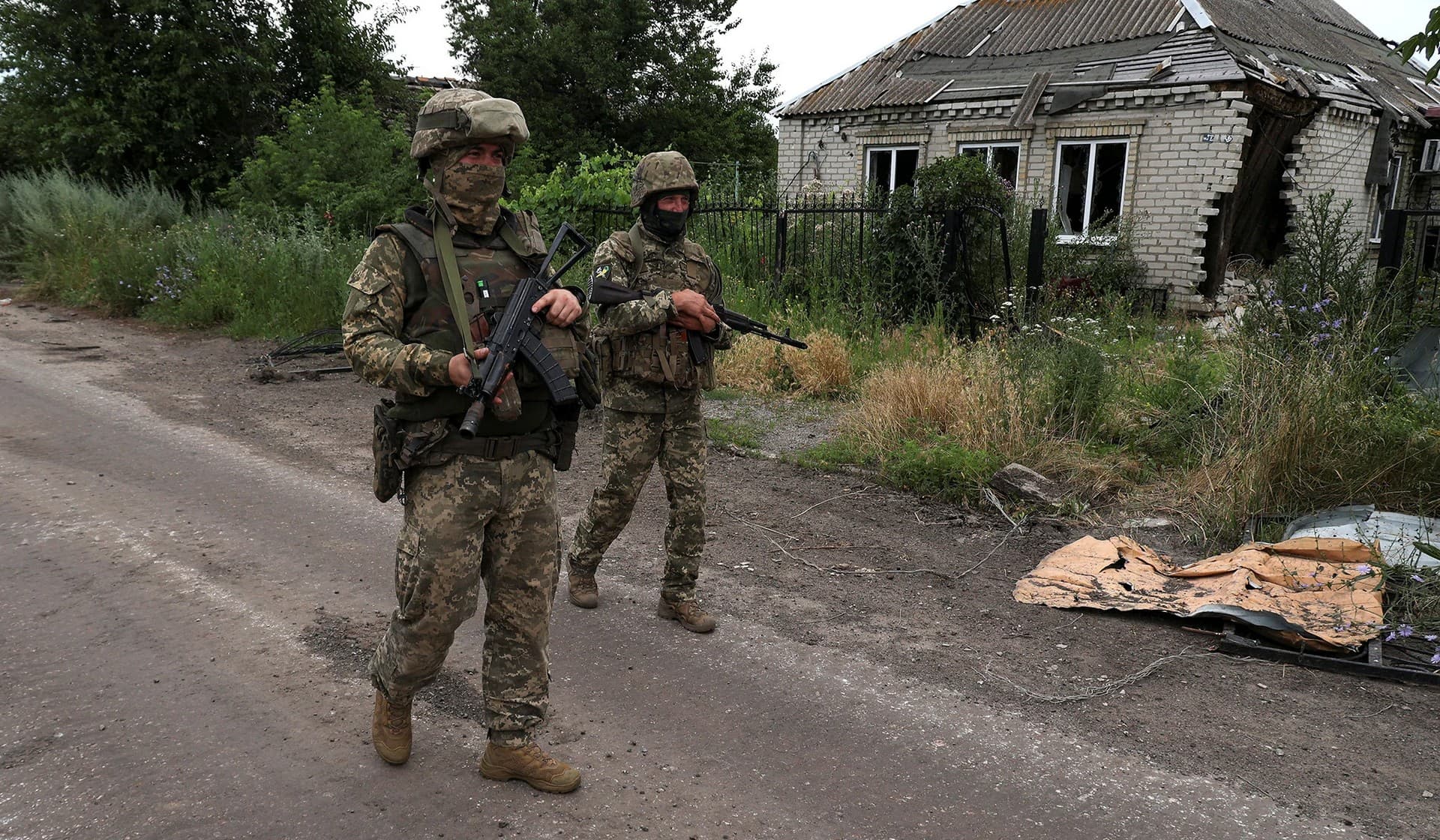 Ukrainian servicemen walk past a house damaged by a Russian military strikes in the village of Vremivka