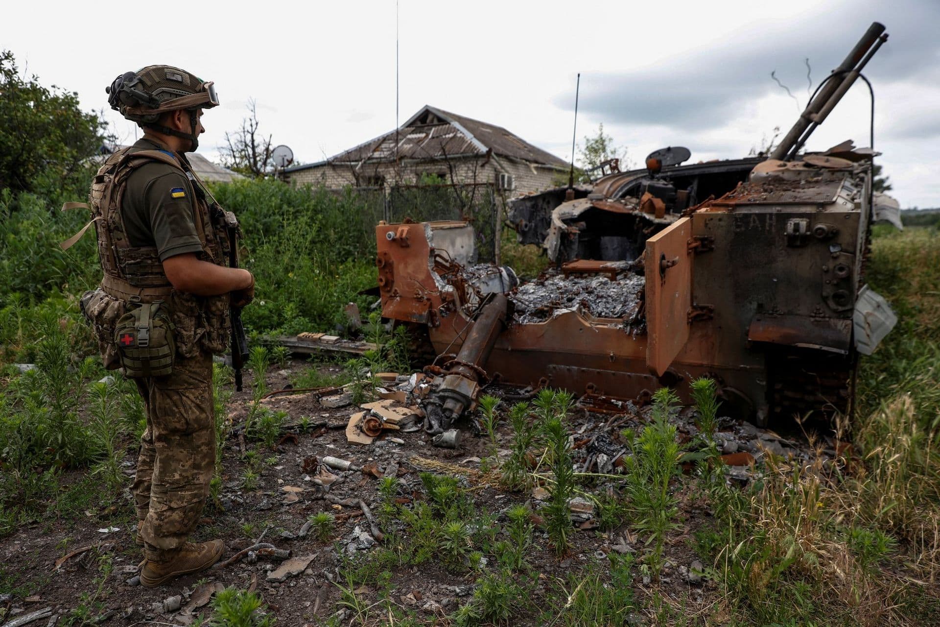 A Ukrainian soldier views the remains of a Russian armored personnel carrier