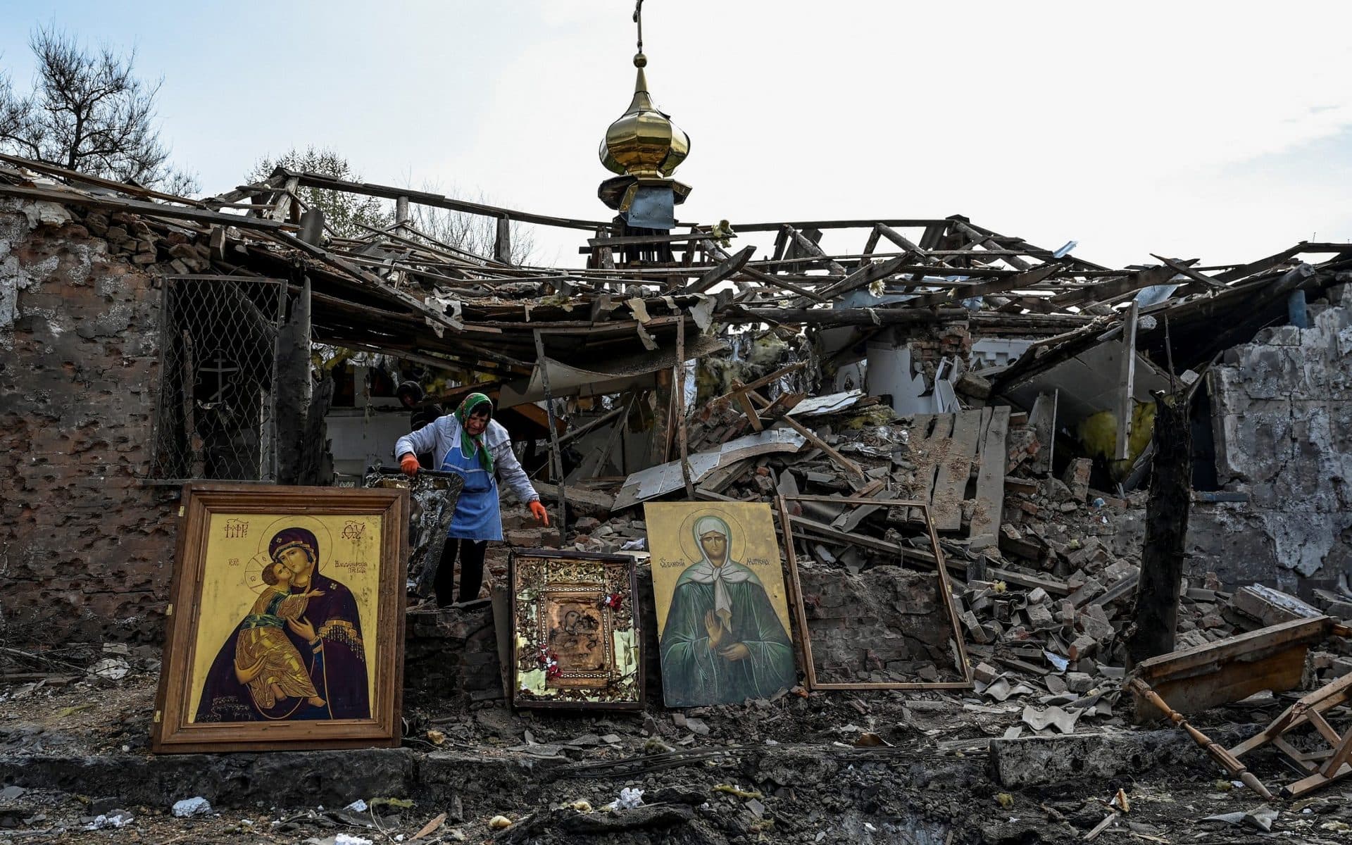 A woman collects Orthodox icons at the site of a church destroyed by a Russian missile strike in the village of Komyshuvakha