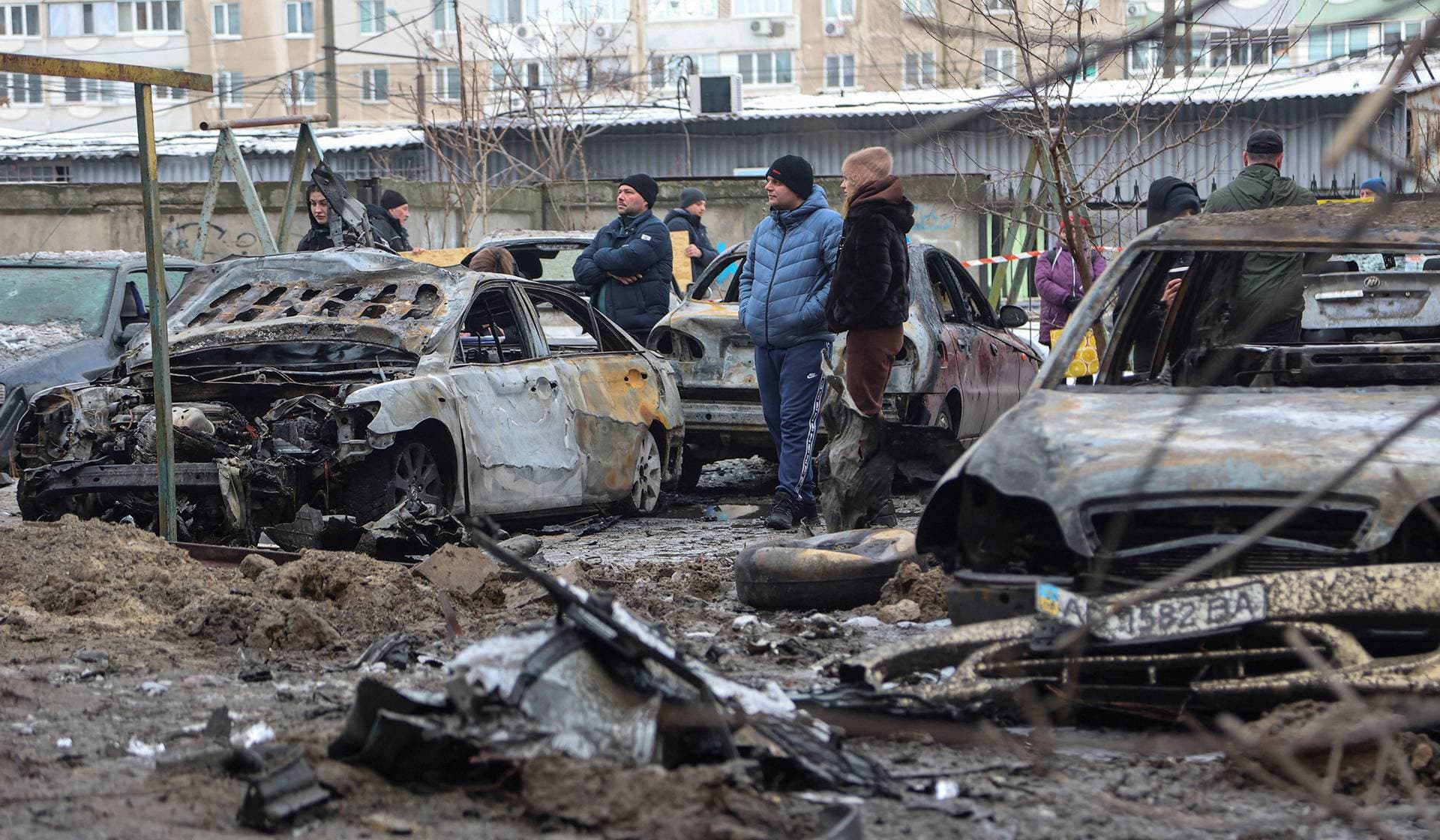 Residents stand next to burned cars at the site of an apartment building damaged during overnight Russian drone and missile strikes in Zaporizhzhia