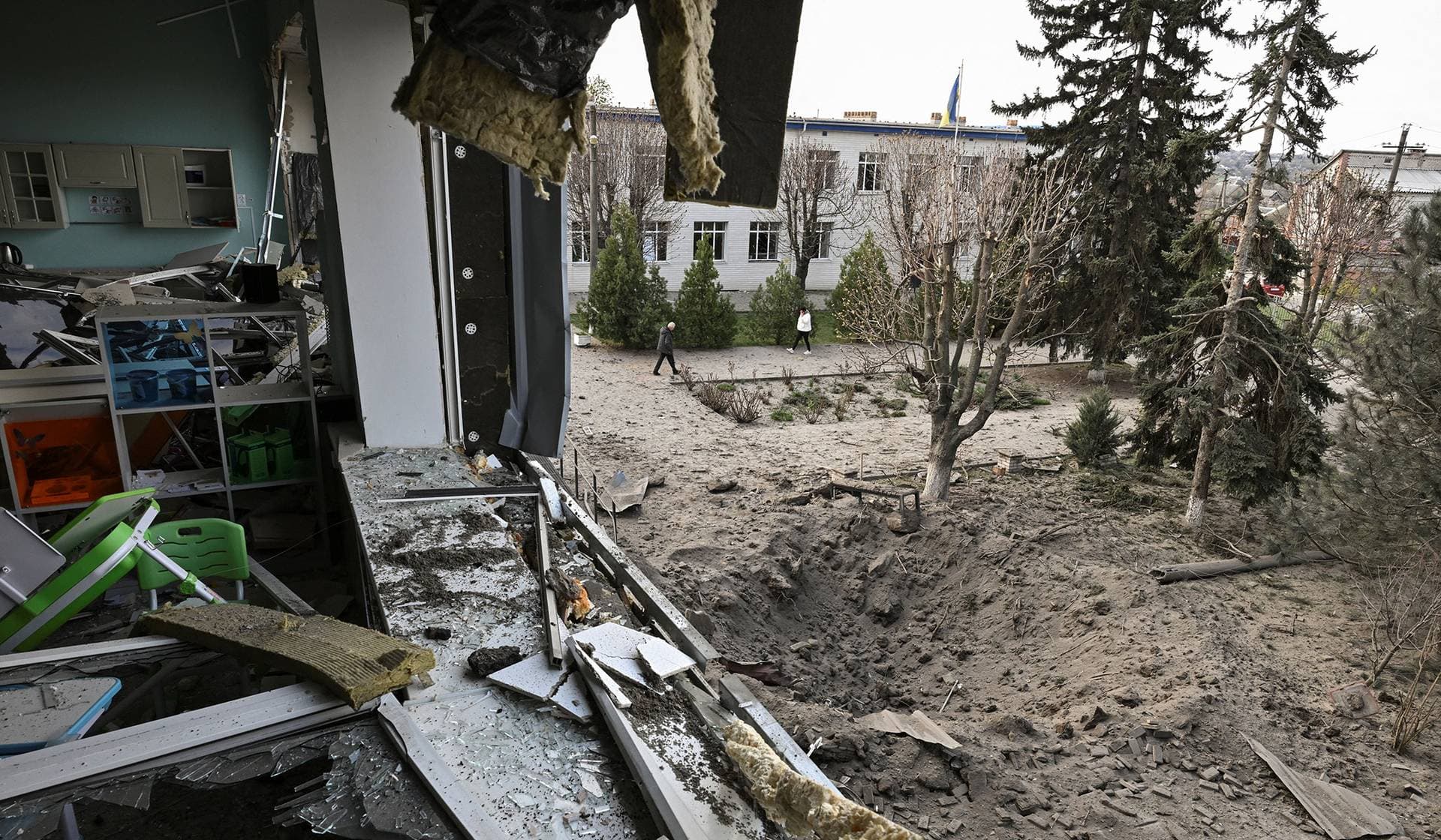 Employees walk next to a crater that appeared at a compound of a school after a Russian air strike on the outskirts of Zaporizhzhia