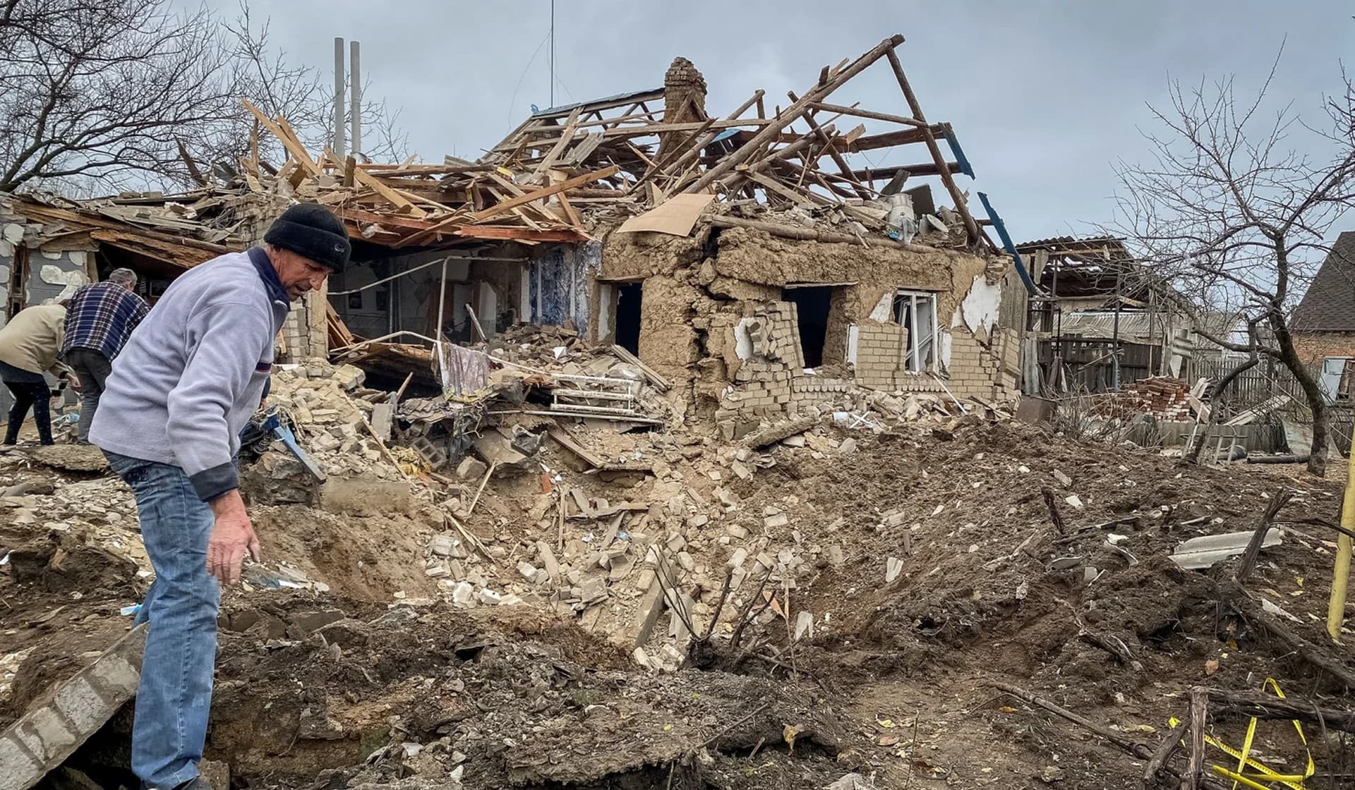 Local residents inspect a crater left by a Russian military strike in the village of Komyshuvakha
