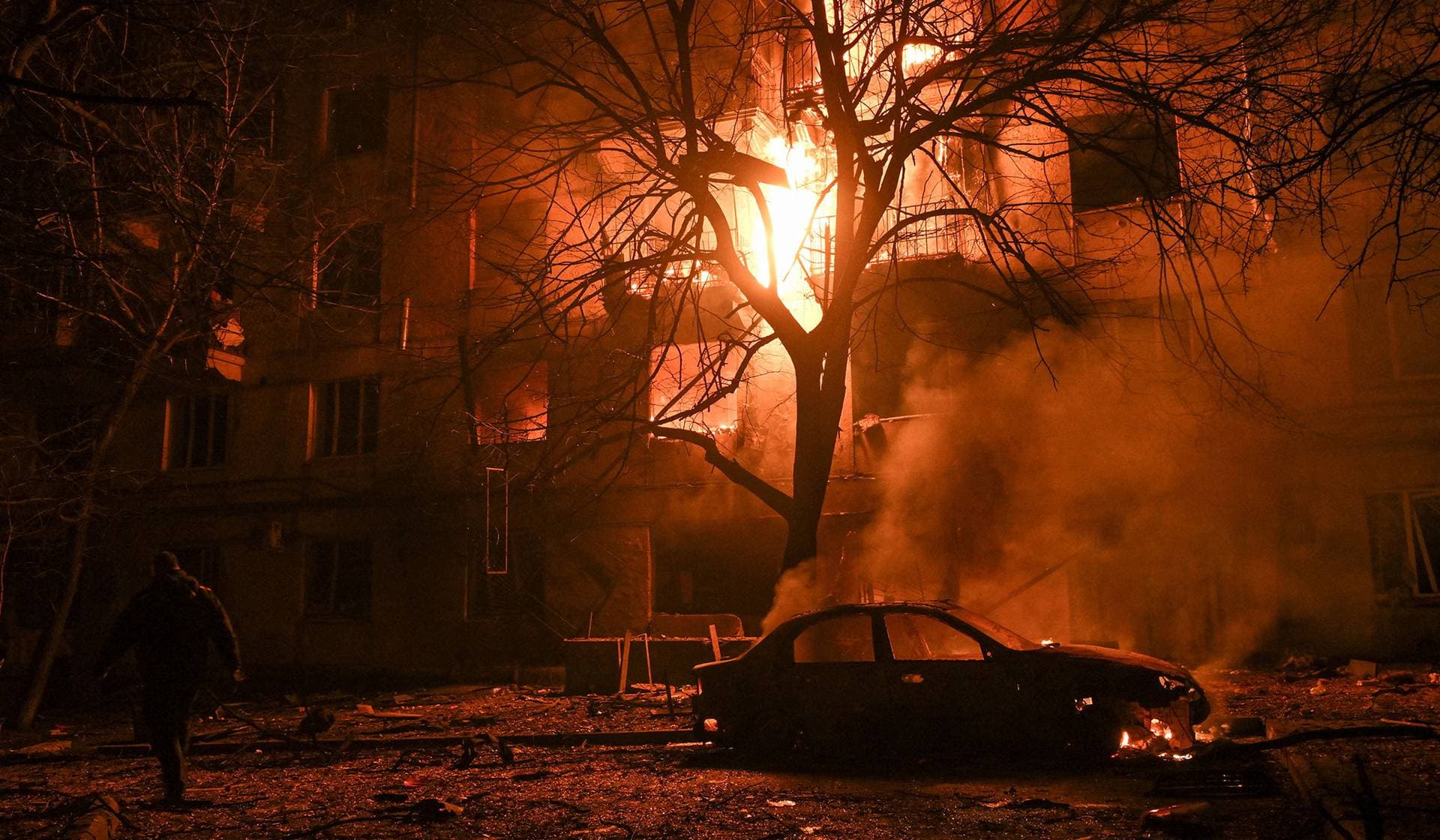 A resident walks in front of a burning apartment building which was damaged during an evening Russian drone strike in Zaporizhzhia