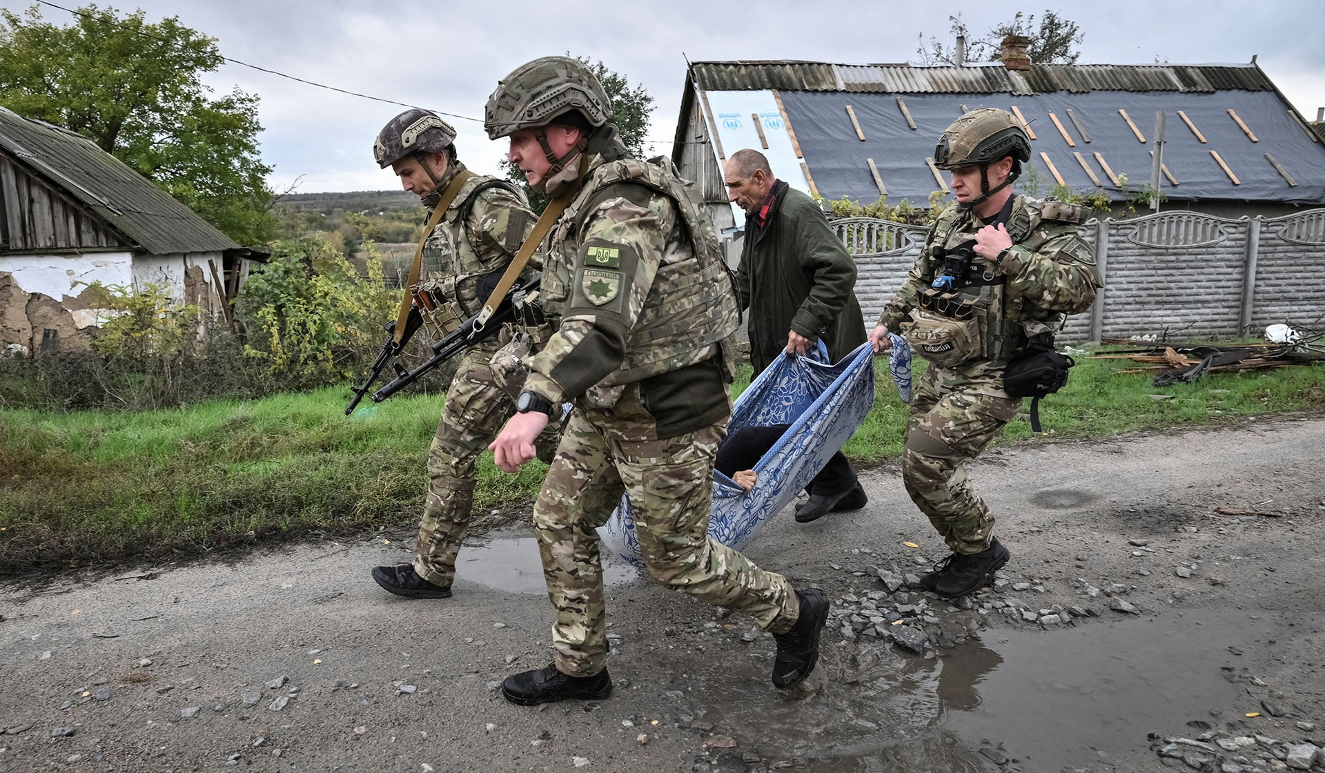 Police officers evacuate a resident from the frontline rural settlement Komyshuvakha