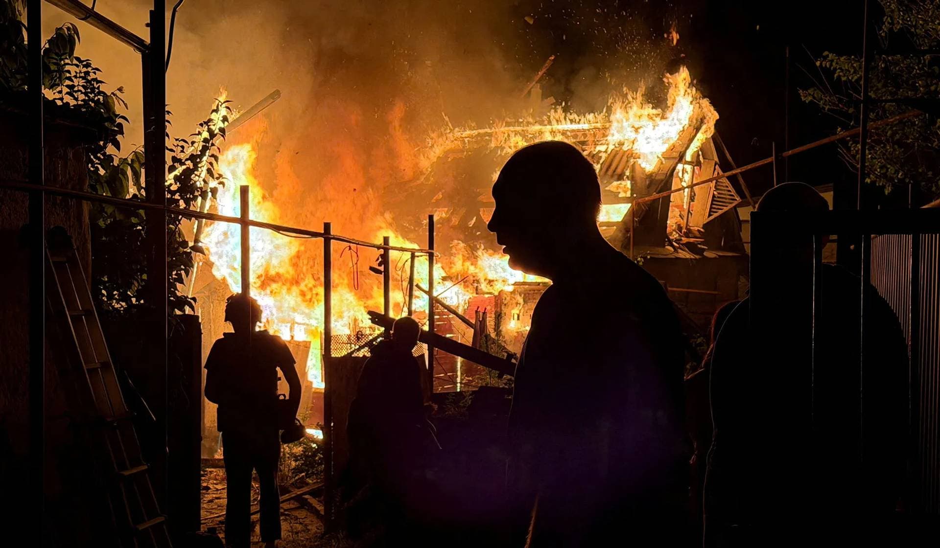 Residents look at a private house that burns after an overnight Russian drone strike in Zaporizhzhia