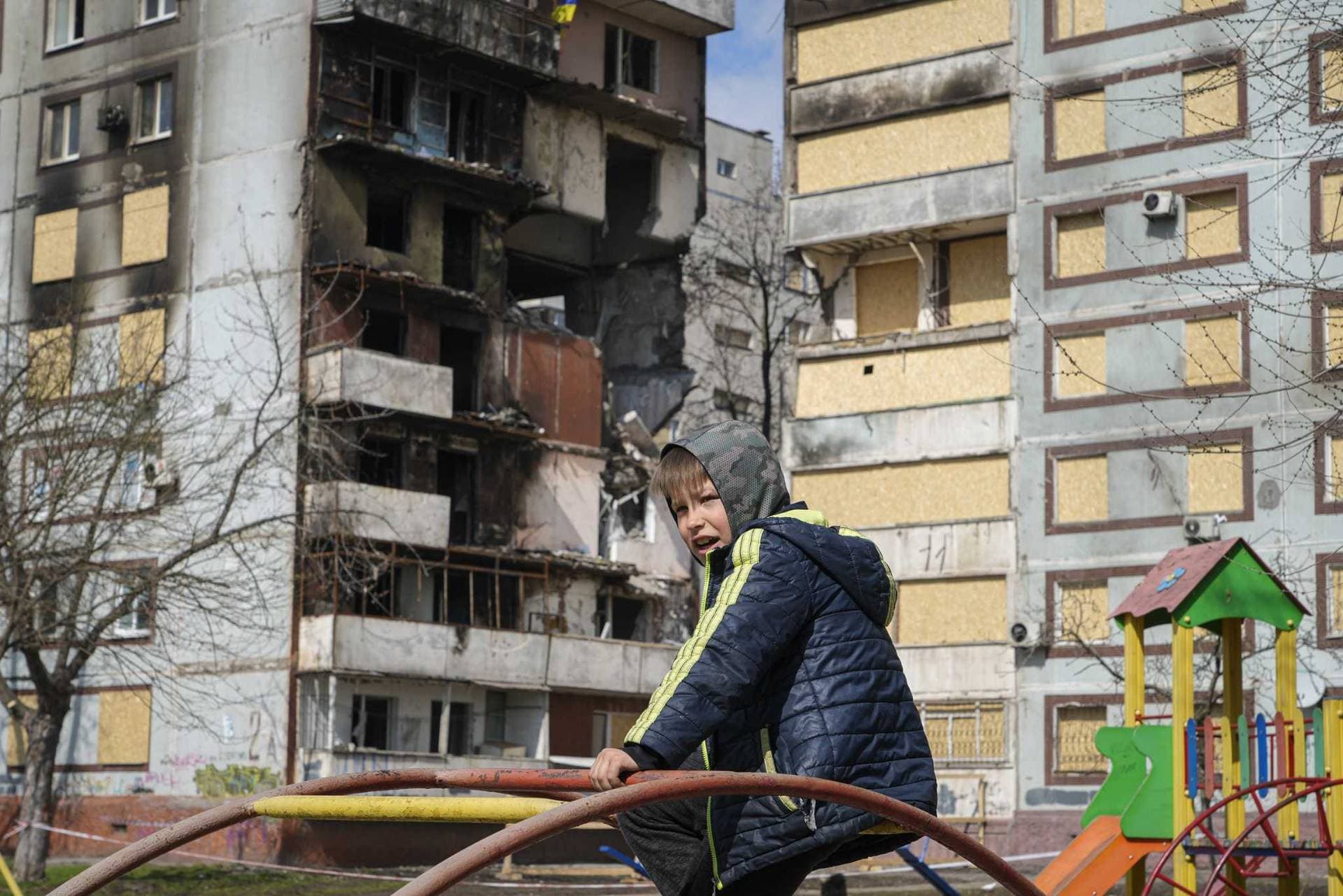 A boy sits on a climbing frame in a playground in front of missile-damaged buildings in Zaporizhzhia